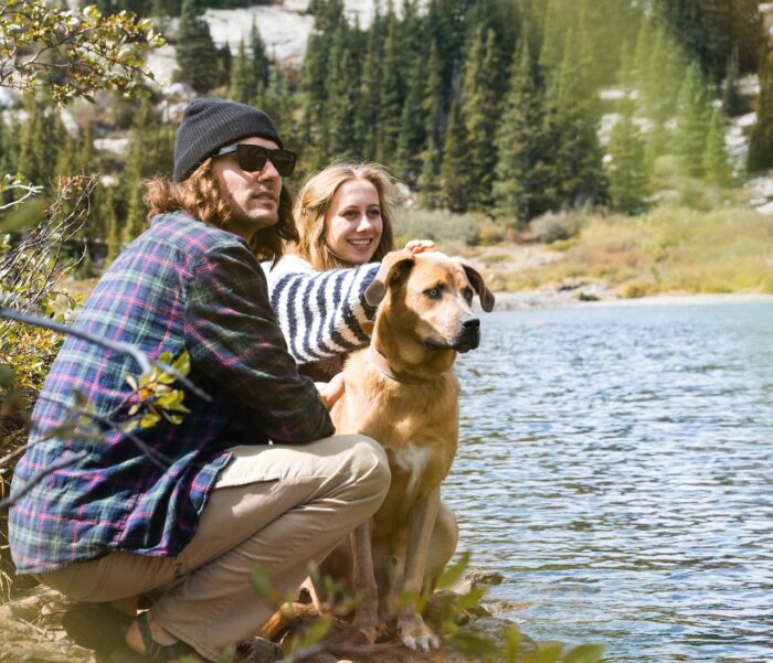 a couple and their dog sit by a river, discussing how human behavior impacts dog behavior